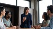 © Eve - Confident female leader conducting corporate training seminar with diverse multiethnic business team around modern conference table for professional growth and employee skill development.