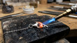 © Digion - Professional goldsmith uses a blue torch flame to melt and solder a metal link on a silver chain necklace within a craft workshop where handmade jewelry creation requires high levels of precision