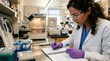 © Felix - Scientist working in laboratory, writing notes on notebook, holding vial, wearing safety glasses