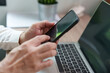© eggeeggjiew - Close-up of a person using a smartphone beside an open laptop at a desk, showing mobile communication, online browsing, digital technology, remote working, multitasking and modern lifestyle.