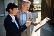 © Davor - Two business professionals reviewing report on smartphone outside office
