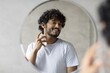 © Prostock-studio - Happy Young Man Of Asian Descent Smiling While Applying Cologne In Front Of Mirror At Home. Taking Care Of Personal Hygiene And Grooming Routine In Comfortable Indoor Setting.