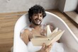 © Prostock-studio - Smiling Young South Asian Man Enjoying Time Reading Book While Relaxing In Bathtub Filled With Foam, Giving A Cheerful Expression In A Comfortable Bathroom Setting.