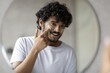 © Prostock-studio - Smiling Young Male Of Indian Descent Applying Facial Cream In Front Of Mirror At Home, Taking Care Of His Skin. Engaged In Daily Skincare Routine, Promoting Healthy Lifestyle And Self-care.
