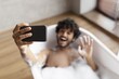 © Prostock-studio - Happy Male With Light Skin And Curly Hair Taking Selfie While Relaxing In Bathtub Filled With Bubbles, Enjoying Peaceful Moment At Home, Capturing Joyful Expression In Bathroom. Relaxation Concept.