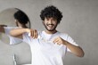 © Prostock-studio - Happy Young Man With Curly Hair Applying Toothpaste On Toothbrush In Bathroom, Engaged In Oral Hygiene Routine, Standing In Front Of Mirror. Wellness Concept.
