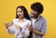 © Prostock-studio - Joyful Young Woman And Man Engaged In Exciting Activity While Looking At Smartphone Together In Studio Setting With Yellow Background. Smiling, Happy, Togetherness, Technology Concept.