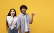 © Prostock-studio - Happy Young Multiracial Couple Expressing Excitement By Smiling And Pointing Towards A Yellow Background, Radiating Joy Together In A Fun And Playful Moment, Celebrating Good News.