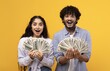 © Prostock-studio - Excited Expression On Faces. Happy Young Man And Woman Holding Wads Of Cash At Studio With Yellow Background. They Are Thrilled And Celebrating Financial Success. Business Concept.