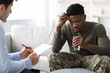 © Prostock-studio - Worried Black Male Patient Sitting On Couch While Discussing Mental Health With Therapist In Office Setting. Holding Glass Of Water, Showing Concern And Seeking Support. Healthcare Concept.