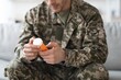 © Prostock-studio - Concerned Young Male Soldier Holding Prescription Medication Bottle While Sitting On Couch At Home. Expressing A Sense Of Care And Attention To Health In A Comfortable Living Room Setting.