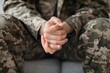 © Prostock-studio - Focused Emotion. Unrecognizable Soldier In Camouflage Uniform Sitting With Hands Together In A Thoughtful Pose At Military Setting. Strength And Discipline Concept.