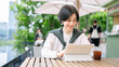 © dodotone - Beautiful smiling adult business asian woman relax at outdoor terrace of cafe with coffee drink and digital tablet on table