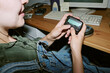 © AnnaStills - Young adult Caucasian woman holding retro pager at office desk with vintage computer, communicating in nineties style. Image suitable for nostalgic tech marketing campaigns