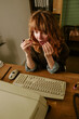 © AnnaStills - Vertical image of shocked young adult Caucasian woman looking at retro computer screen in vintage office, representing workplace stress or data error in corporate communication