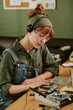 © AnnaStills - Vertical image of young Caucasian woman wearing headphones while repairing vintage CD player in retro office, representing retro technology restoration and electronics repair services