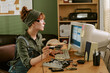 © AnnaStills - Young adult Caucasian woman technician repairing hardware in retro office, using soldering iron and looking at CRT monitor. Image suitable for vintage Information Technology support marketing