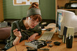 © AnnaStills - Young adult Caucasian woman wearing safety glasses soldering computer hardware in retro office. Image represents vintage technology repair and is suitable for Information Technology service marketing