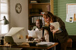 © AnnaStills - Diverse young adult colleagues, African American man and Caucasian woman, reviewing documents in retro office. Image represents vintage corporate communication and teamwork
