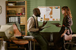 © AnnaStills - Diverse middle aged colleagues discussing paperwork in retro office setting. Image represents vintage corporate communication and is suitable for nostalgic business marketing campaigns