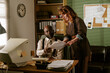 © AnnaStills - Middle aged African American man and young adult Caucasian woman working in retro office, reviewing paper documents. Image suitable for vintage corporate communication