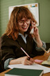 © AnnaStills - Young adult Caucasian woman working in retro office, talking on landline telephone and writing notes. Image suitable for vintage corporate communication campaigns, vertical