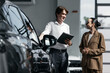 © wedmoments.stock - Man helping a woman choose a new car in a showroom, representing auto dealership and professional sales consultation.