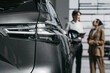 © wedmoments.stock - Modern car in focus in the foreground while a consultant talks with a female customer in a dealership.