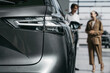 © wedmoments.stock - Female customer speaking with a car dealer beside a modern vehicle in a showroom. Concept automotive sales, consultation and vehicle selection.