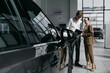 © wedmoments.stock - Salesperson showing a female customer the interior and features of a new car in a modern dealership.