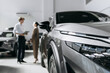 © wedmoments.stock - Modern car in focus in the foreground while people discuss a vehicle purchase in a dealership. Concept car sales and vehicle selection.