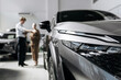 © wedmoments.stock - Modern vehicle displayed in a showroom with customers and a salesperson discussing the purchase.