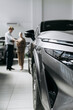© wedmoments.stock - New car in focus at a dealership while customers explore available vehicles. Concept automotive sales and vehicle selection.