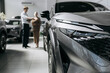 © wedmoments.stock - New car in focus inside an automotive showroom with potential buyers nearby. Concept vehicle purchase and dealership services.