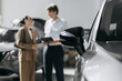© wedmoments.stock - Modern car displayed prominently while a salesperson advises customers in a dealership. Concept vehicle selection and customer service.