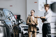 © wedmoments.stock - Car dealership specialist helping a woman select a new vehicle using digital information.