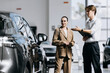 © wedmoments.stock - Man and woman examining a modern car while discussing its features and purchase options.