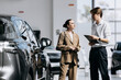 © wedmoments.stock - Salesperson explaining a car to a female customer before purchase in a modern automotive showroom.