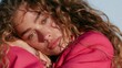 © Raul - Close up portrait of a young woman with curly hair resting her head on her hand while wearing a bright pink jacket outdoors.