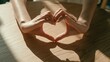 © Khaisan - Woman's hands forming a heart shape, symbol of love and care, with soft light and shadow