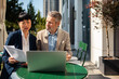 © Davor - Two business colleagues reviewing documents on laptop at outdoor cafe