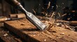 © Nusrat - Hand held sharp metal chisel carving deep groove into rustic wooden board with flying sawdust fragments captured in action shot within professional furniture workshop.