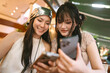 © dodotone - Happiness two young asian women using cell phone hanging out with friends shared experience Bangkok trip moment