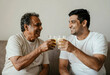 © Pixel-Shot - Intergenerational bonding and family connection, senior father and adult son toasting with orange juice glasses at home for health and wellness celebration