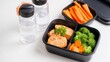 © liliyabatyrova - A neatly organized lunch showcases grilled salmon, bright broccoli, and crisp carrot sticks in black containers. Clear bottles of water complete this balanced meal preparation, perfect for any day