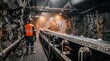 © extrude - Worker in orange safety gear inspecting underground mining conveyor belt.