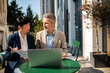 © Davor - Two business professionals reviewing documents with laptop at outdoor cafe