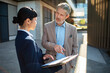 © Davor - Senior manager and colleague reviewing report outside office
