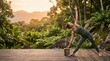 © Sadia - Outdoor yoga practice in tropical jungle, woman performing triangle pose on wooden deck, serene morning wellness and fitness concept