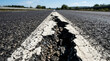 © peno - Commercial stock photo of a deep wide crack splitting a black asphalt road on a white line. Ground-level close-up of damaged highway infrastructure, pothole repair need, and asphalt texture.